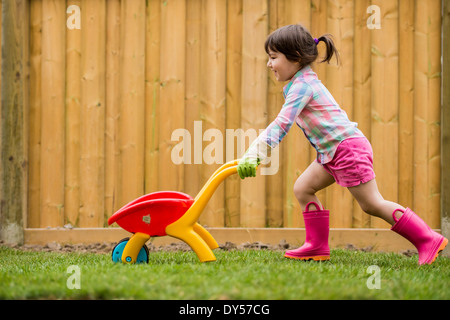 Junges Mädchen mit Spielzeug Schubkarre im Garten Stockfoto