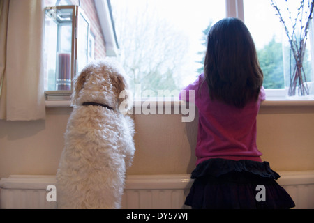 Mädchen und ihr Hund stehen und blickte aus dem Fenster Stockfoto