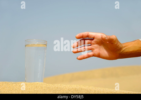 Hand ist bei einem frischen Glas kaltes Wasser in der Wüste erreichen. Stockfoto