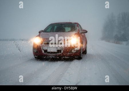 Auto mit Scheinwerfern auf der Fahrt entlang der nebligen Schnee bedeckt Straße Stockfoto