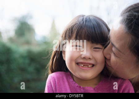 Mädchen wird von ihrer Mutter im Garten auf die Wange geküsst Stockfoto