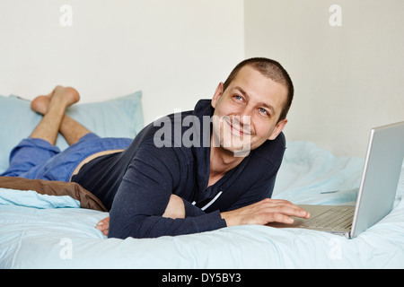 Mitte erwachsenen Mannes auf Bett mit laptop Stockfoto