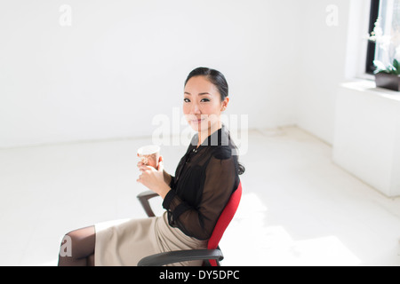 Junge Frau sitzt auf Bürostuhl mit Kaffee Stockfoto