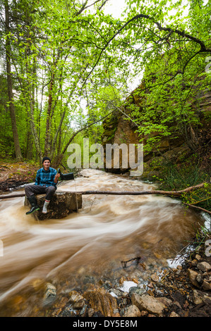 Männliche Wanderer sitzen auf überfluteten Flussfelsen, Naramata, British Columbia, Kanada Stockfoto