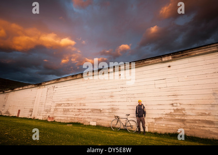 Junger Mann stand neben weißen Wand mit seinem Fahrrad Stockfoto