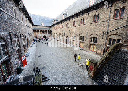 Glockenturmhof Brügge Belgien | BRÜGGE, Belgien — Besucher durchqueren den umschlossenen Hof der Hallen, den mittelalterlichen Markthallen, die den Sockel des Glockenturms von Brügge an der Südseite des Marktes bilden. Der um 1240 begonnene und bis ins späte 13. Jahrhundert erweiterte Belfort-Hallen-Komplex umfasst etwa 36.576 Quadratfuß (3.396 Quadratmeter) und diente einst als überdachter Marktplatz und Lagerhaus, das für die Handelswirtschaft der Stadt von zentraler Bedeutung war. Stockfoto