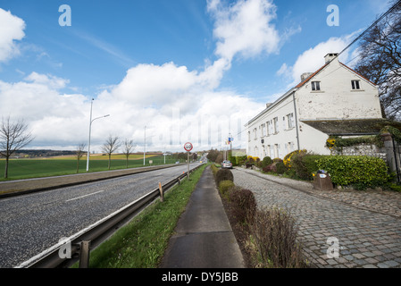 Ferme du Caillou Napoleons Bauernhaus Vieux-Genappe Belgien | VIEUX-GENAPPE, Belgien — Die weiße Ziegelfassade der Ferme du Caillou steht neben einer modernen Autobahn, die sich zum Horizont erstreckt. Napoleon Bonaparte richtete am Abend des 17. Juni 1815 sein letztes Hauptquartier in diesem Bauernhaus ein und kam über die alte Charleroi-Brüssel-Straße — die N5 — die der angrenzende Asphalt nachzeichnet, etwa 4 Meilen (6,4 km) südlich des Löwenhügels an. Es war dieselbe Angriffsroute, die die französische Armee genommen hatte, um den Koalitionsstreitkräften des Herzogs von Wellington auf dem Schlachtfeld vor ihnen zu begegnen. Stockfoto