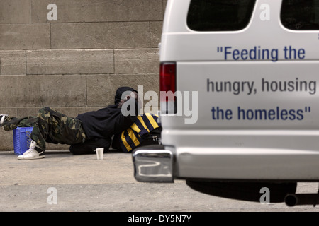 Schwarzer Rüde auf dem Bürgersteig und Van mit dem Worte, die die Hungrigen ernähren und die Obdachlosen unterbringen Stockfoto