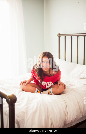 Junge Frau sitzt mit gekreuzten Beinen auf Bett Stockfoto