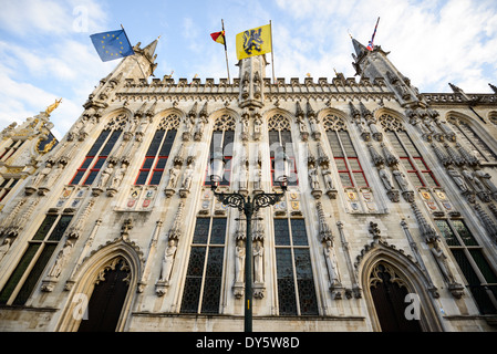 BRÜGGE, Belgien — die gotische Fassade des Brügge Rathauses (Stadhuis) aus dem Jahr 1376 erhebt sich dramatisch gegen den Himmel. Die aufwendige architektonische Dekoration des Gebäudes umfasst Statuen und Wappenschilde, die Gebiete darstellen, die historisch von Brügge aus regiert wurden. Dieses Meisterwerk der mittelalterlichen Bürgerarchitektur ist eines der ältesten Rathäuser in den Niederlanden. Stockfoto