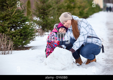 Glückliche Mutter mit Tochter sitzen zusammen im Schnee im Winter park Stockfoto