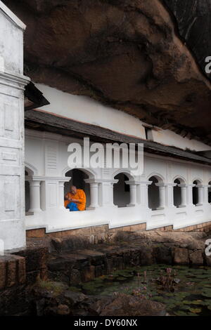 Ein Mönch schaut auf sein Handy unter Schutz, Royal Rock Temple, goldenen Tempel von Dambulla, der UNESCO, Dambulla, Sri Lanka Stockfoto