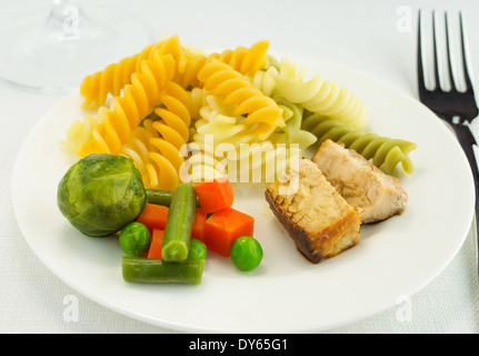 Pasta mit Gemüse und Fisch auf dem Teller. Nächsten Gabelung und einem Glas Wein Stockfoto