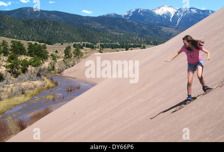 Sandboarder reitet auf einer Düne über Medano Creek auf die Burg Creek Picnic Area im Great Sand Dunes National Park 8. Mai 2009 in Mosca, Colorado. Stockfoto