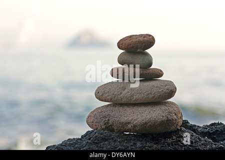 Steinen Pyramide auf Sand als Symbol für Zen, Harmonie und Balance. Ozean im Hintergrund Stockfoto