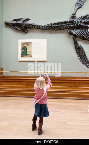 Kind und Dinosaurier; ein junges Kind ein Foto von Dinosaur fossilen Knochen, Natural History Museum London UK Stockfoto