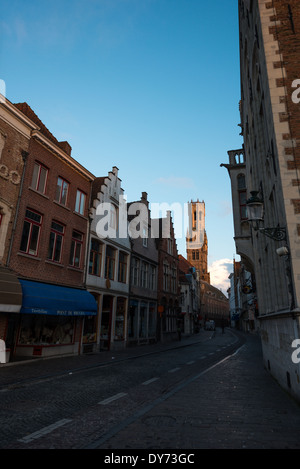 BRÜGGE, Belgien - der Glockenturm von Brügge fängt die Morgensonne in der Ferne ein, hinter einer Kopfsteinpflasterstraße, die im historischen Zentrum von Brügge, Belgien, noch immer im Schatten liegt. Mittelalterliche Architektur und ruhige Kanäle prägen das Stadtbild von Brügge, oft als „Venedig des Nordens“ bezeichnet. Brügge gehört zum UNESCO-Weltkulturerbe und bietet Besuchern eine Reise in die Vergangenheit Europas mit seinen gut erhaltenen Gebäuden und kopfsteingepflasterten Straßen, die die reiche Geschichte der Stadt widerspiegeln. Stockfoto