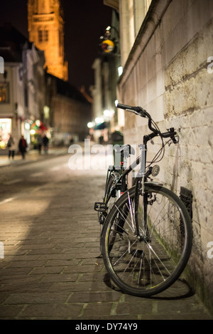 BRÜGGE, Belgien – Ein einsames Fahrrad lehnt sich nachts an eine historische Gebäudemauer im mittelalterlichen Zentrum von Brügge. Die Szene fängt die Mischung aus modernem Transport und erhaltener Architektur ein, die charakteristisch für diese UNESCO-Weltkulturerbe-Stadt ist. Traditionelle Straßenbeleuchtung sorgt für ein stimmungsvolles Abendambiente entlang der historischen Straßenlandschaft. Stockfoto