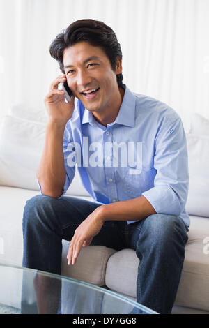 Glücklicher Mann sitzt auf der Couch am Telefon sprechen Stockfoto