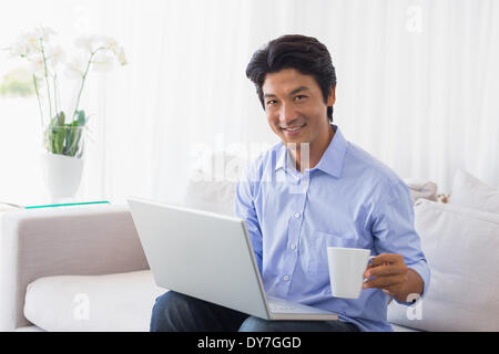 Glücklicher Mann auf Couch mit Laptop Kaffeetrinken Stockfoto