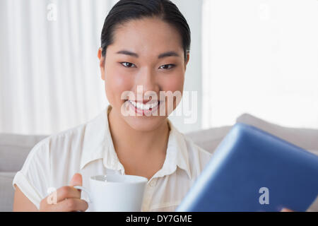 Lächelnde Frau sitzen auf Couch mit Tablet-pc mit Kaffee Stockfoto