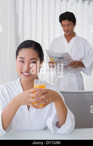 Frau im Bademantel mit Orangensaft mit Freund im Hintergrund Stockfoto