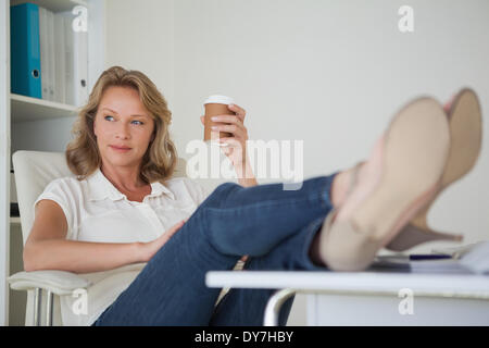 Lässige Geschäftsfrau mit einem Kaffee mit ihren Füßen oben am Schalter Stockfoto