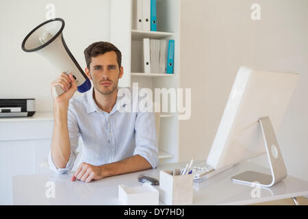 Lässige Geschäftsmann sitzt am Schreibtisch mit Megaphon Stockfoto