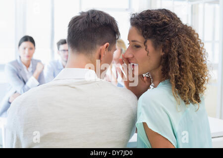 Lässige Geschäftsfrau telling ein Geheimnis an Kollegen Stockfoto