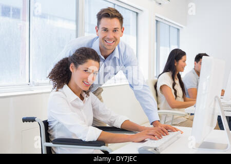 Lässige Geschäftsfrau im Rollstuhl mit Kollegen an ihrem Schreibtisch arbeiten Stockfoto