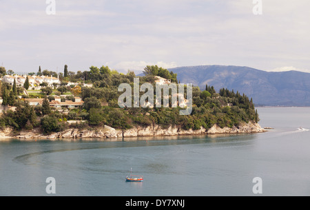 Kalami Bucht, Korfu, von der Südseite, mit neuen Ferienhäuser auf der Klippe und einem traditionellen Fischerboot bei der Arbeit gesehen. Stockfoto