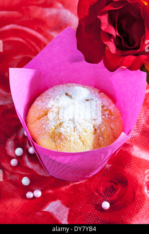 Muffin in rosa Wickel, Rosen blühen und Zucker Perlen auf rotem Blumenmuster Stockfoto