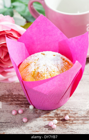 Muffin in rosa Wickel, rosa Blüte, Tasse und Zucker Perlen auf Holztisch Stockfoto