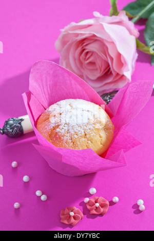 Muffin in rosa Wickel, rosa Blüte, Tasse und Zucker Perlen auf rosa Grund Stockfoto