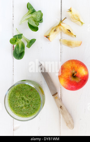 Glas von Apfel Feldsalat Smoothie, Apfel, Küchenmesser und Feldsalat auf weißer Holztisch Stockfoto
