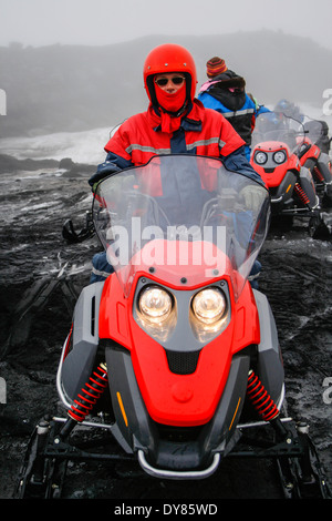 Mann mit rotem Helm und Schal mit roten Motorschlitten während eine Schneemobil-Tour auf einem Gletscher in Island Stockfoto