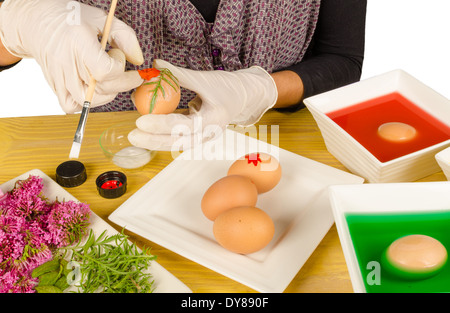 Hände, die Dekoration Ostern Eiern Blätter und Blumen, während einige andere färben Stockfoto