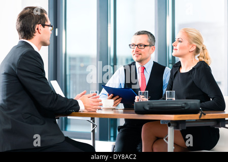 Business - junger Mann in einem Job-Interview, übergibt seine Bewerbungsunterlagen an den Chef und seine Assistentin in ihrem Büro Stockfoto