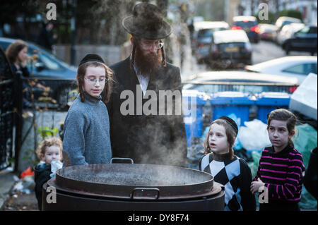 London, UK - 9. April 2014: Mitglieder der jüdischen Gemeinde von Stamford Hill zu bringen, Besteck, Töpfe, Pfannen und Geschirr, koscher in kochendem Wasser in Vorbereitung für Pessach. Nach der Thora da es verboten ist, Essen Chametz (gesäuertes Essen) während Pessach, Utensilien die Chametz, Berührung haben kann getaucht werden in kochendem Wasser (Hagalat Keilim) um sie von jeglichen Spuren von Chametz zu bereinigen, die im Laufe des Jahres angesammelt haben kann. Bildnachweis: Piero Cruciatti/Alamy Live-Nachrichten Stockfoto