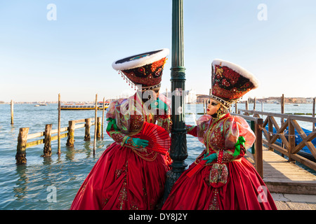 Karneval in Venedig - zwei Frauen in schönen roten Kostüme, Masken und Hüte Pose von der Lagune, Carnevale di Venezia, Italien Stockfoto