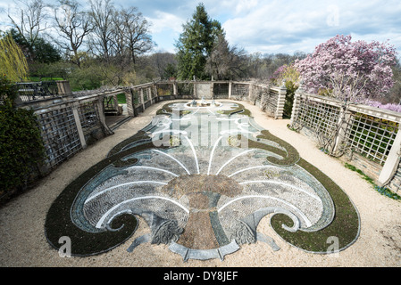 Dumbarton Oaks Gardens Landscape Design Washington DC | WASHINGTON D.C., Vereinigte Staaten – Ein Muschelmosaik aus Kieselsteinen verankert die Fountain Terrace bei Dumbarton Oaks, dem Landschaftsplaner Beatrix Farrand aus Georgetown, der ab 1921 entworfen wurde. Farrand und der Besitzer Mildred Barnes Bliss, selbst beschriebene „Gartenzwillinge“, arbeiteten das Gelände mehr als drei Jahrzehnte lang in einem Beaux-Arts-Rahmen, in dem Arts and Crafts ausführlich darlegte, dass das National Register Farrand als unübertroffen in seiner Karriere bezeichnet. Eine blühende Magnolie markiert die Frühlingssaison der Terrasse. Stockfoto