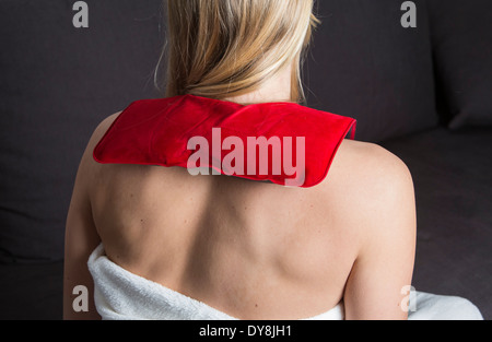 Junge Frau hat Rückenschmerzen, Nackenschmerzen, wärmt sich mit einem Nackenkissen, gefüllt mit einem Schlammgewicht Stockfoto