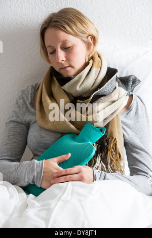 Junge Frau in Schmerzen, lindert die Schmerzen im Zusammenhang mit einer Wärmflasche Stockfoto