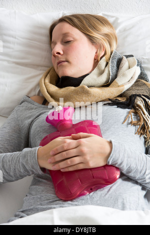 Junge Frau in Schmerzen, lindert die Schmerzen im Zusammenhang mit einer Wärmflasche Stockfoto