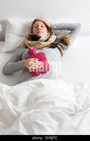 Junge Frau in Schmerzen, lindert die Schmerzen im Zusammenhang mit einer Wärmflasche Stockfoto