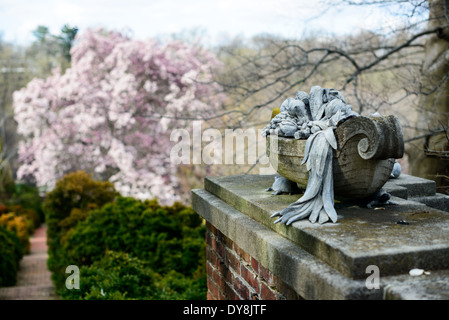 Dumbarton Oaks Gardens Stone Sculpture Washington DC | WASHINGTON D.C., Vereinigte Staaten – auf einer Gartenmauer bei Dumbarton Oaks befindet sich Eine mit Skulpturen übersäte Urne aus Stein, die mit Obst und Laub überflutet ist. Die Landschaftsarchitektin Beatrix Farrand behandelte solche Ornamente eher als integralen Bestandteil des Gartendesigns als als zufällige Dekoration und arbeitete mit dem Gutsbesitzer Mildred Barnes Bliss zusammen, um ab 1921 skulpturale Stücke entlang wichtiger Sichtlinien zu platzieren. Stockfoto