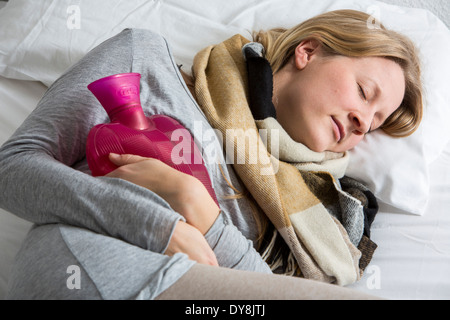 Junge Frau in Schmerzen, lindert die Schmerzen im Zusammenhang mit einer Wärmflasche Stockfoto