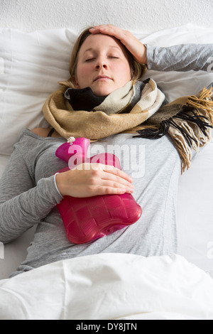 Junge Frau in Schmerzen, lindert die Schmerzen im Zusammenhang mit einer Wärmflasche Stockfoto