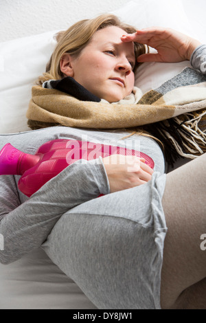 Junge Frau in Schmerzen, lindert die Schmerzen im Zusammenhang mit einer Wärmflasche Stockfoto