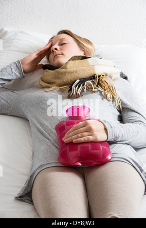 Junge Frau in Schmerzen, lindert die Schmerzen im Zusammenhang mit einer Wärmflasche Stockfoto